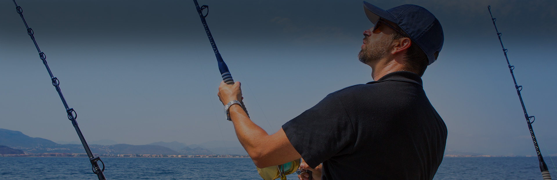 Fishing rods and reels positioned on the stern of a charter boat with churning blue ocean water in the background, suggesting an active deep sea fishing expedition